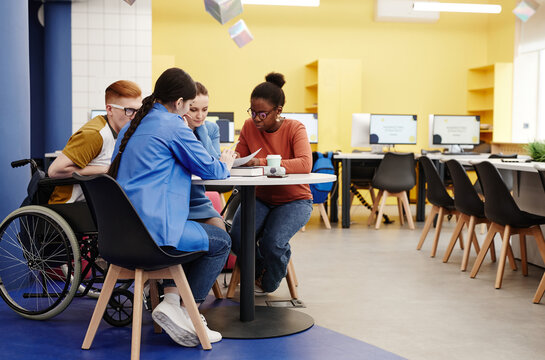 Vibrant full length shot of diverse group of students studying together at table in college lab, copy space