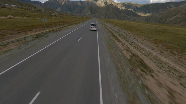 Aerial view white minibus driving on highway at picturesque sunny mountain valley freedom landscape. FPV sports drone freestyle flying at minivan movement on roadway wilderness