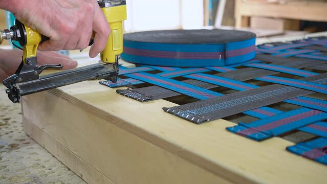 Stapling elastic band with a yellow pneumatic stapler. Furniture manufacture.