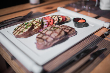 A plate of grilled beef meat with grilled slices of potatoes, tomatoes and onions