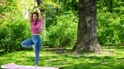 Happy young woman practice yoga in green garden outdoor in open air, wearing pink t-shirt and blue...