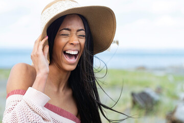 Pretty African American woman with black hair wearing a floppy hat at the ocean beach