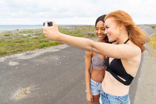 African American woman with long black hair and redhead woman with freckles outside on ocean beach road together