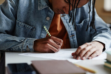 Closeup of black young man writing in notebook at desk in school classroom or in college