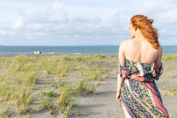 Redhead woman with freckles wearing dress at ocean beach.