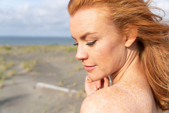 Redhead woman with freckles wearing dress at ocean beach.