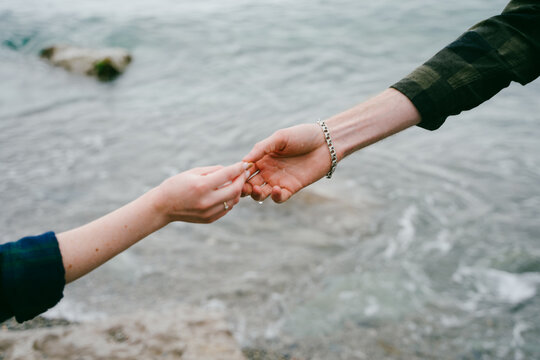The hand of a girl and a guy reach out to each other on the seashore.