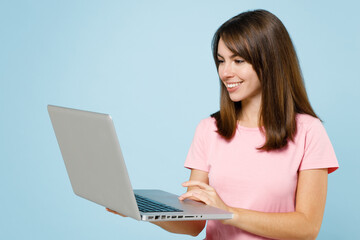 Fototapeta premium Young smiling freelancer happy caucasian woman 20s wearing pink t-shirt hold use work on laptop pc computer isolated on pastel plain light blue background studio portrait. People lifestyle concept