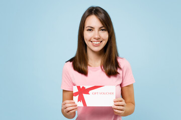 Young smiling happy caucasian woman 20s in pink t-shirt look camera hold gift certificate coupon...