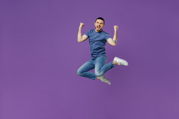 Full body young overjoyed excited cool man 20s wearing basic blue t-shirt jump high do winner gesture clench fist isolated on plain purple color background studio portrait. People lifestyle concept.