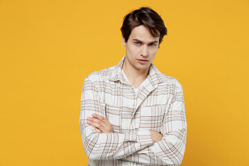 Young serious attractive calm caucasian man 20s wearing white casual shirt hold hands crossed folded look camera isolated on plain yellow background studio portrait. People lifestyle emotions concept.