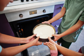Mother with kids cooking at kitchen, happy children's moments. Cheesecake in the oven.