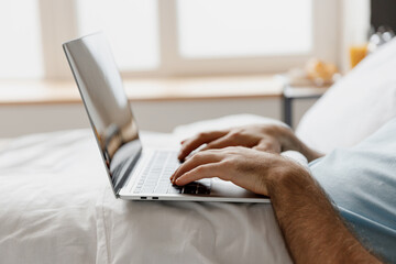 Naklejka premium Close up cropped freelancer man lying in bed hold use working on laptop pc computer typing message rest relax spend time in bedroom lounge home in own room house wake up dream. Remote jobs concept