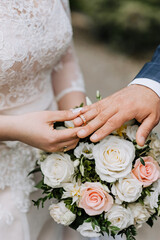 Obraz na płótnie Canvas Hands, fingers with gold rings of the bride and groom close-up at the wedding ceremony against the background of a bouquet of roses. Wedding photography, portrait, concept.