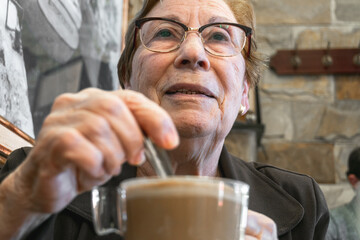 Close-up of an older woman with glasses having a latte.