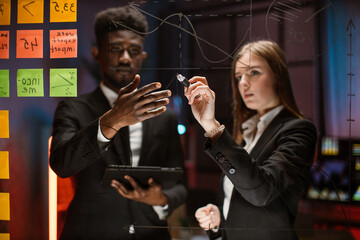Planning strategy. Blurred shot of group of two young multiethnic people in formal wear, planning on a glass board. Caucasian lady writing on the board African American man. Focus on the board