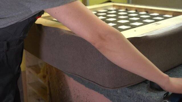 Furniture upholstery. A carpenter fixes the fabric with a pneumatic stapler.