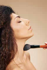 Obraz premium Profile close up portrait of enjoyed adorable tanned awesome curly Latin lady hold makeup brush on shoulder apply highlighter satisfied posing isolated on pastel beige background close eyes. Banner