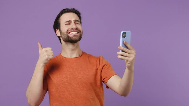 Young brunet bearded man 20s in red t-shirt get video call use mobile cell phone talk conducting pleasant conversation greet with hand isolated on plain pastel light purple background studio portrait