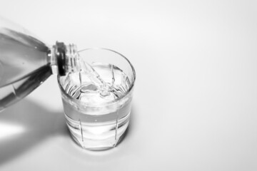 Pouring water into a glass from a plastic bottle close-up. Black and white photo.
