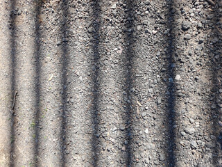 Piso de tierra con piedritas esparcidas, con sol reflejado en una reja produce lìneas de sombra rectas geomètricas, formando un hermoso diseño abstracto natural pata fondos
