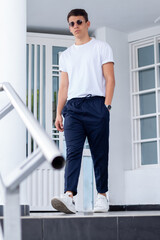 Male latin model wearing black glasses and walking on elegant black stairs place. Model with modern clothes. White shirt and blue pants.