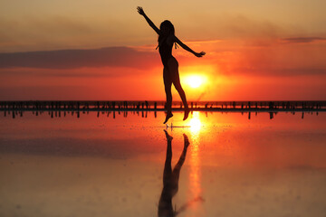 silhouette of a young slim woman in a swimsuit who dancing at sunset on the sea. summer holiday