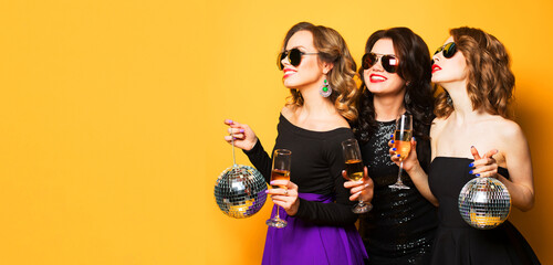 Three joyful charming young women friends with disco balls drinking champagne and having fun...