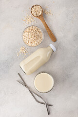 A bottle and a glass of plant-based oat milk with an ingredient in a bowl with reusable straws on a...