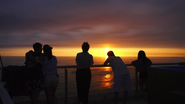 several male and female friends looking at a beautiful purple sunset and taking photos with their cell phones in Punta Hermosa with the sun reflecting on the waves of the sea at golden hour in 4k