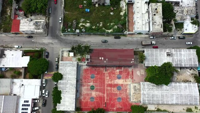 Aerial drone footage looking down on an empty basketball court.  The drone slowly pans up to show the city surrounding it.  