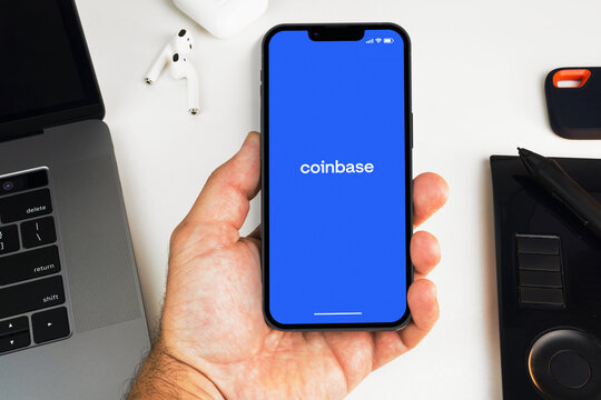Man holding a smartphone with Coinbase exchange app on the screen on white background table. Office environment. Rio de Janeiro, RJ, Brazil. May 2022