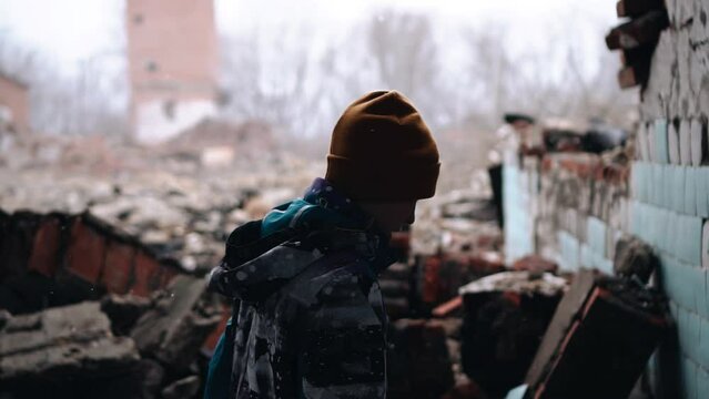 It is snowing and a boy is walking through the ruins of the house, carefully overcoming the ruins.