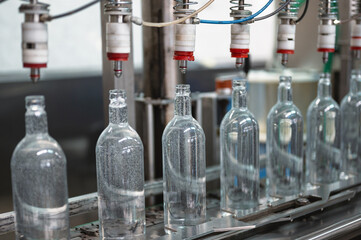 Equipment pours vodka into glass bottles on production line