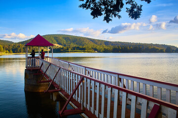 lake with mountains in the background with soft and warm light and clouds in the sky two persons in...