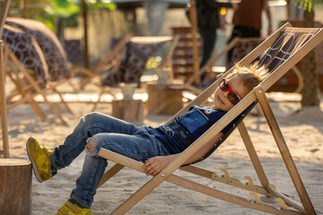 Cute toddler child, boy, sitting on a beach chair in the center of the sity in a cofeteria made to...