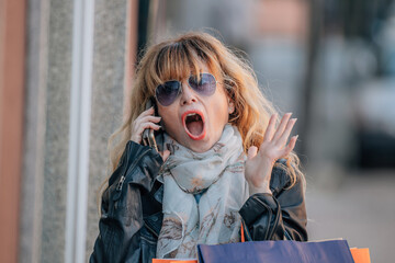middle-aged woman in the street with shopping bags and mobile phone with a surprised expression
