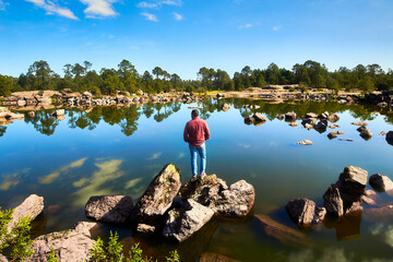young man in front of a lake with a lot of rocks and forest in the background in mexiquillo...