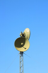 green satellite communication dishes on a mast in the blue sky