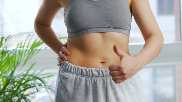 Woman puts on her pants, strokes her stomach and gives a thumbs up. Concept of healthy digestion and bowel function.