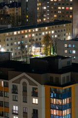 Obraz premium Night panorama of the city. Tall apartment buildings illuminated by night illumination. Top view of windows and roofs of houses