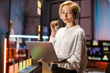 Portrait of pretty cheerful blond Caucasian executive businesswoman wearing headset using laptop,...