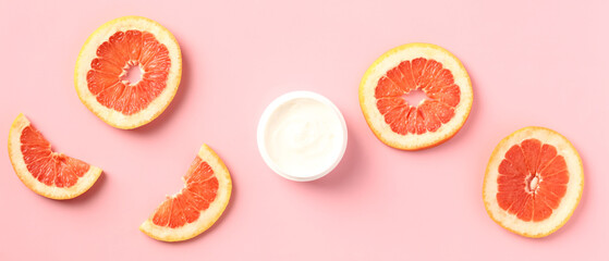Vitamin c body moisturizer cream jar with sliced grapefruit on pink background. Wide banner for...