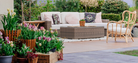 Ogrodowe patio ozdobione ratanową sofą i stolikiem kawowym z fotelem ogrodowym.
Taras wśród zieleni  - obrazy, fototapety, plakaty