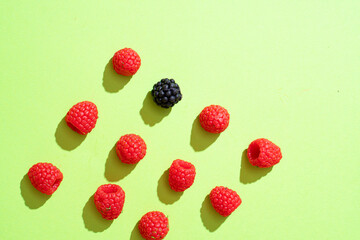 Raspberries and blackberries on a green background are evenly laid out. hard sunlight