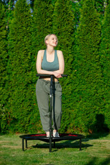 girl does Jumping fitness on trampoline in outdoor on green grass and trees on background