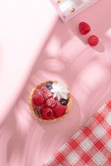 Tartlet with fresh berries in jelly and with meringue on a pink table