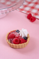 Tartlet with fresh berries in jelly and with meringue on a pink table