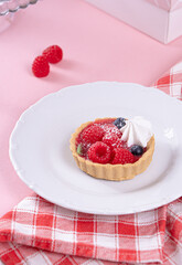 Sandless cake with cream and blueberries, and raspberry on a white plate on a pink table