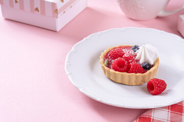 Sandless cake with cream and blueberries, and raspberry on a white plate on a pink table